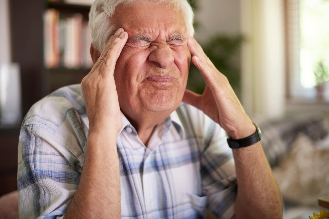 An elderly man grimacing in agony, clutching his head with a pained expression on his face.