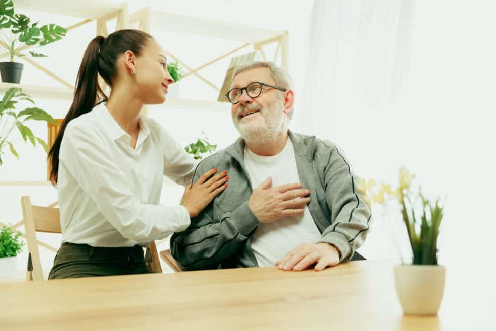 A woman gently holds the hand of an elderly man, showing care and support in their connection.