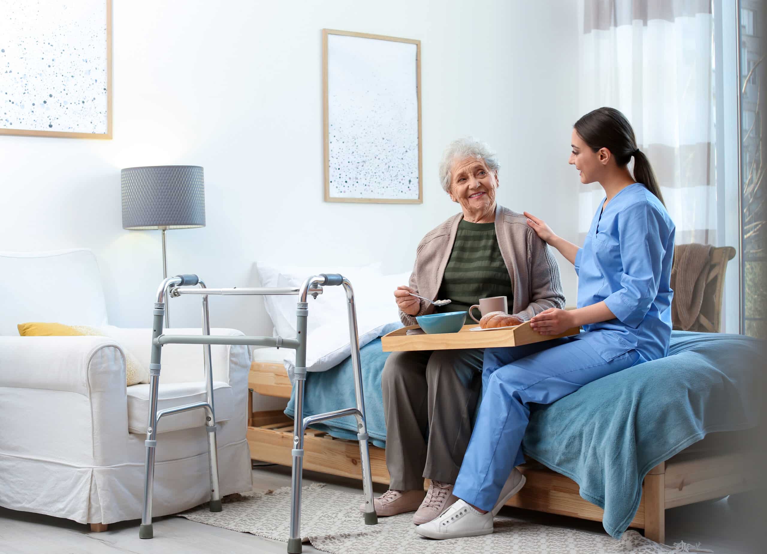 A nurse attentively sits beside an elderly woman on a bed, providing care and support.