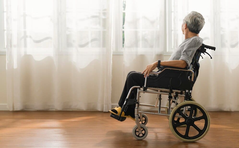  A senior man in a wheelchair, finding solace by the window. We offer specialized services for visually impaired adults.