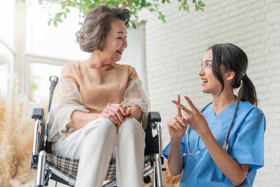 A nurse providing elder care assistance to an elderly woman in a wheelchair.